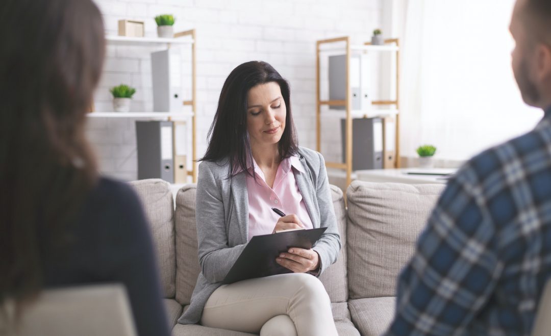 professional psychologist taking notes at couple meeting with patients -